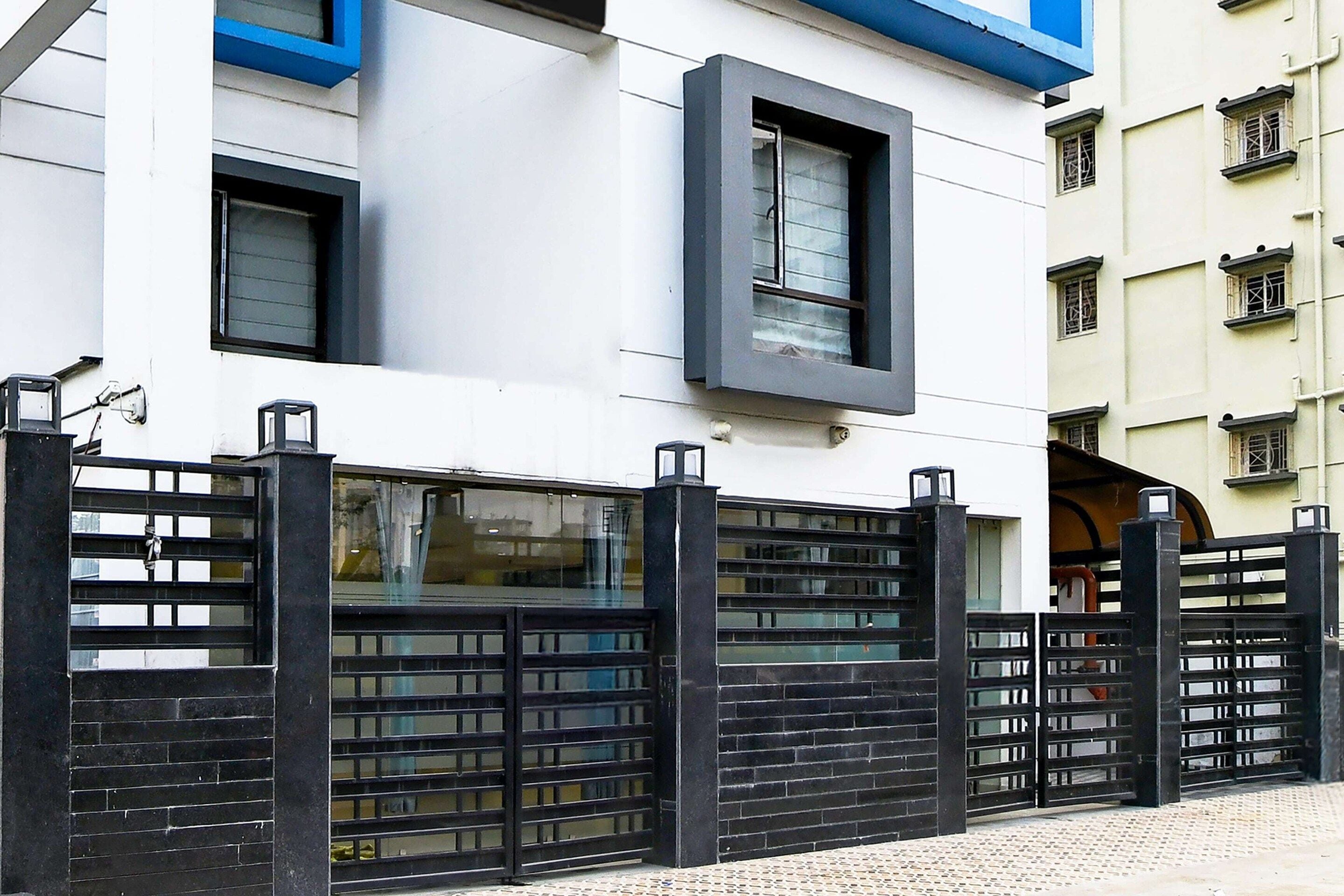 A modern building with a black metal gate, large windows, and a blue accent on the upper floor.
