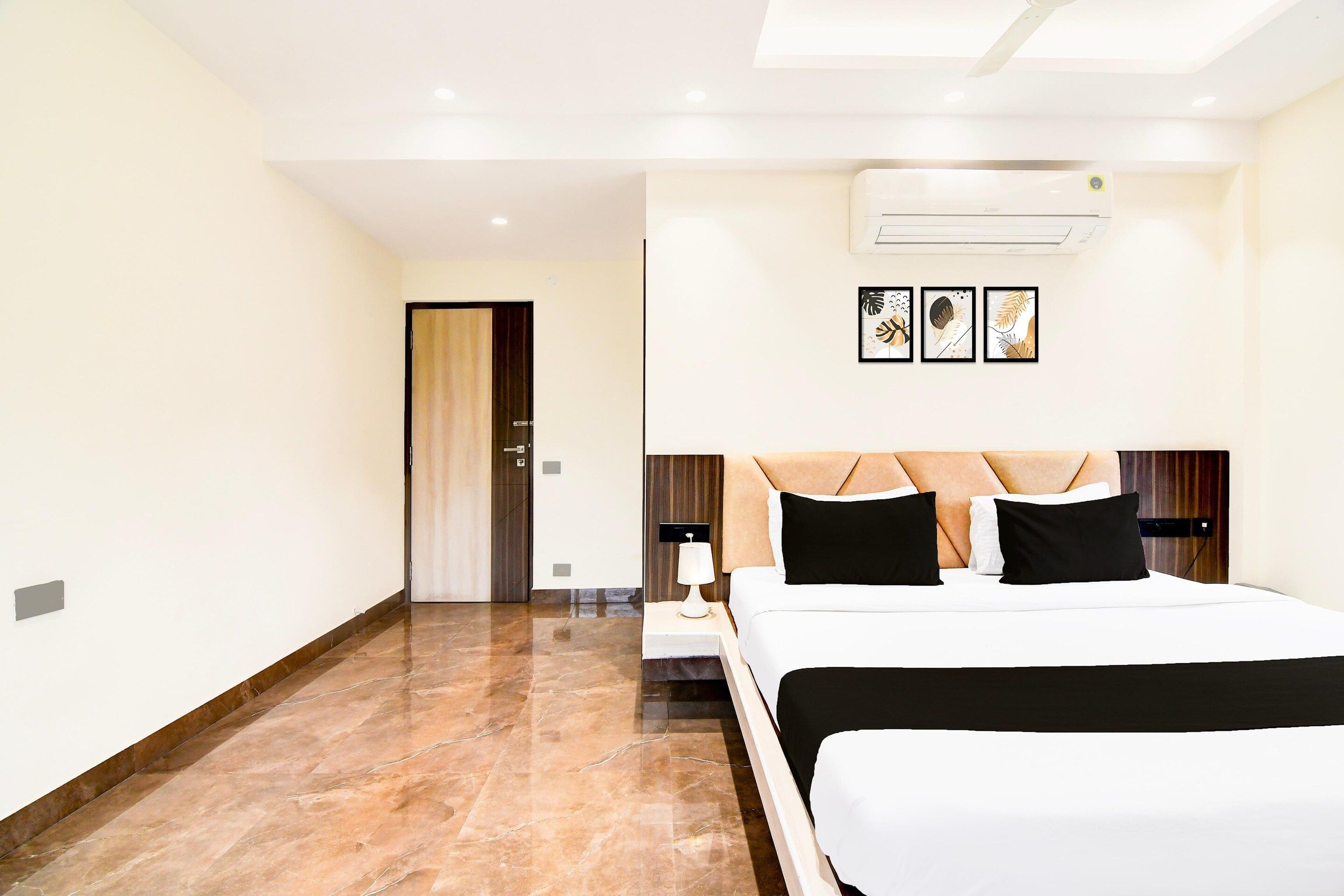 Ein modernes Hotelzimmer mit einem großen Bett, einem Nachttisch, einer Klimaanlage und gerahmten Kunstwerken an der Wand.