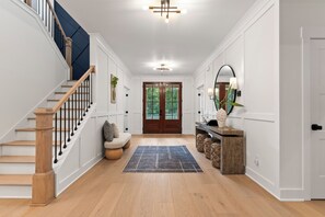 Ein Flur mit einer Holztreppe, einer Bank, einem Teppich und einer zur Außenseite führenden Tür.