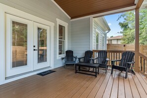 A covered porch with wooden flooring, a table, and four Adirondack chairs. - Luxury Pool & Spa Villa + Golf Cart to Lake Dock (Gainesville)