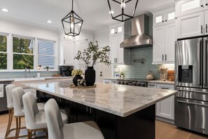 A modern kitchen with a large island, stainless steel appliances, and a view of the outdoors. - Luxury Pool & Spa Villa + Golf Cart to Lake Dock (Gainesville)