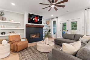 A modern living room with a fireplace, a television mounted above it, and a ceiling fan. - Luxury Pool & Spa Villa + Golf Cart to Lake Dock (Gainesville)