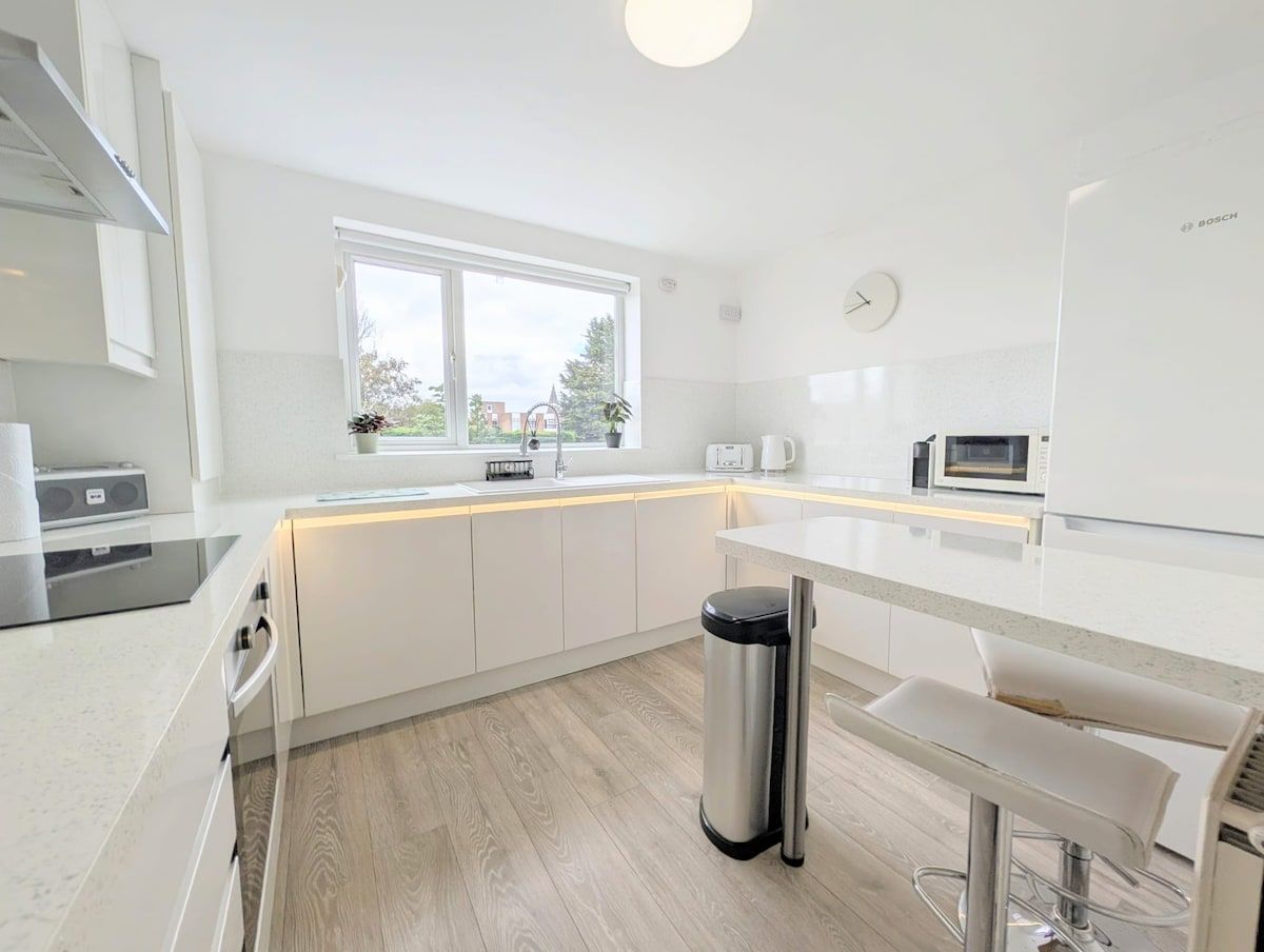 A modern kitchen with white cabinetry, a stainless steel trash bin, a window with a view, and a Bosch microwave.