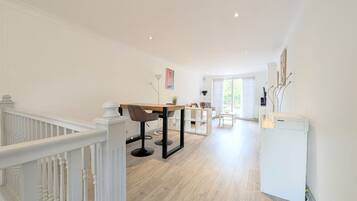 A spacious room with a wooden floor, a dining table with chairs, a white radiator, and a staircase with white railings.