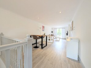 Een ruime kamer met een houten vloer, een eettafel met stoelen, een witte radiator en een trap met witte leuningen.