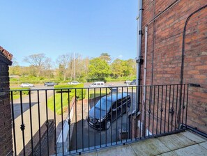 Een balkon met uitzicht op een parkeerterrein en een bakstenen gebouw.