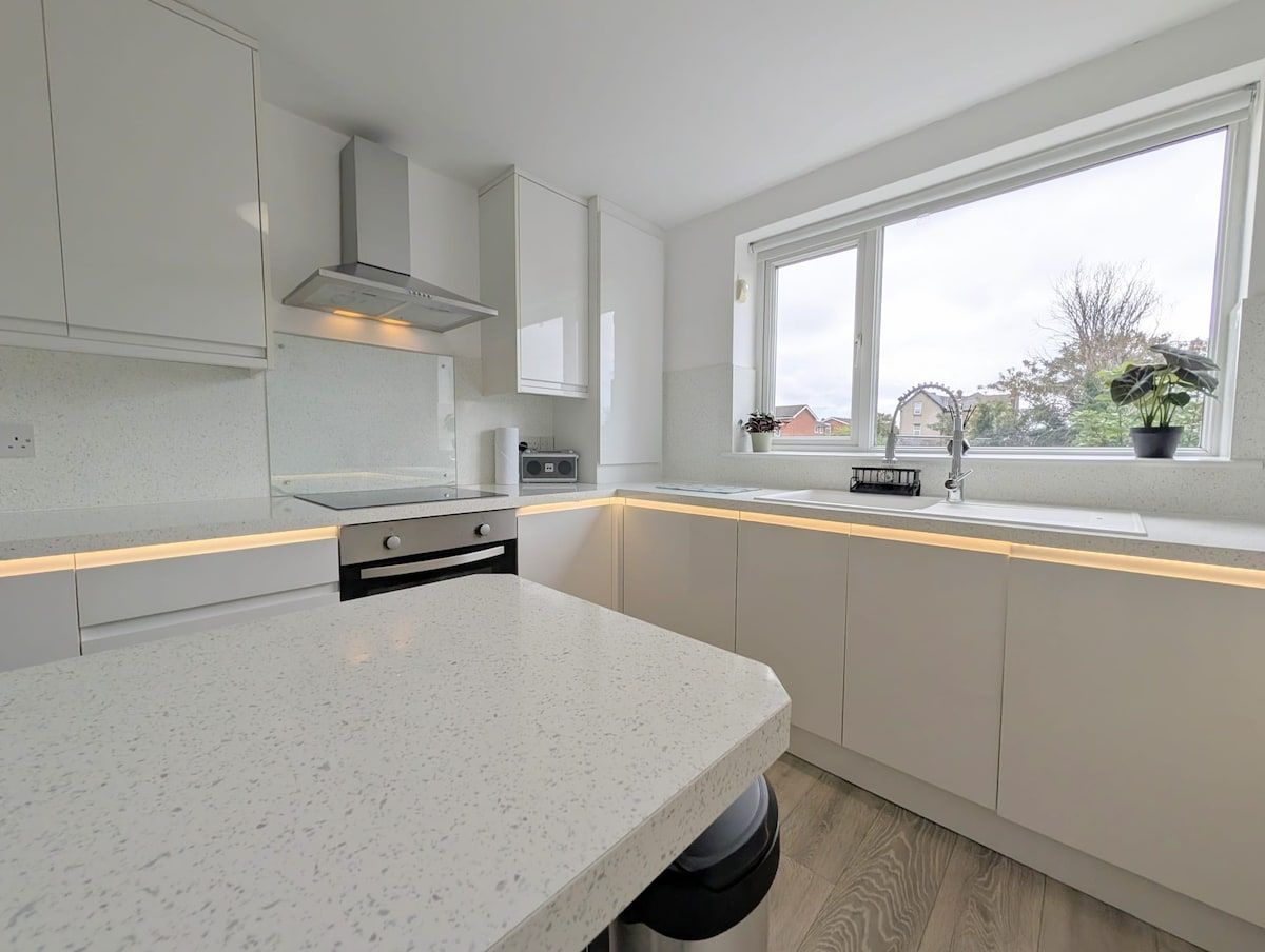 A modern kitchen with white cabinetry, a large window, and a countertop.