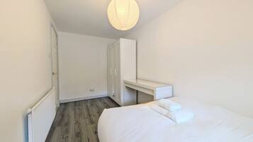 A bedroom with a bed, a bedside table, a wardrobe, and a hanging light fixture.