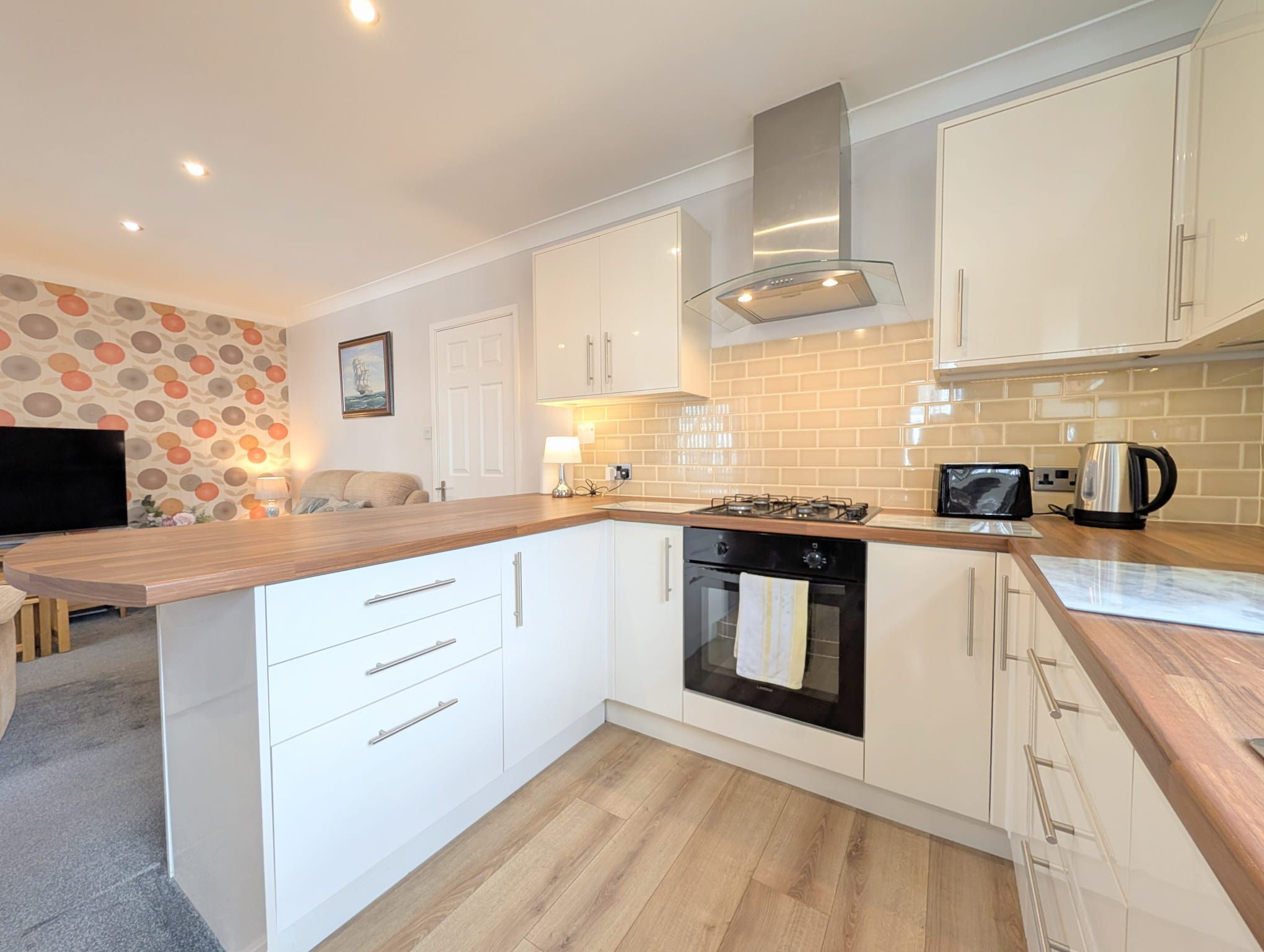 A modern kitchen with white cabinets, a wooden countertop, a gas stove, and a tiled backsplash.