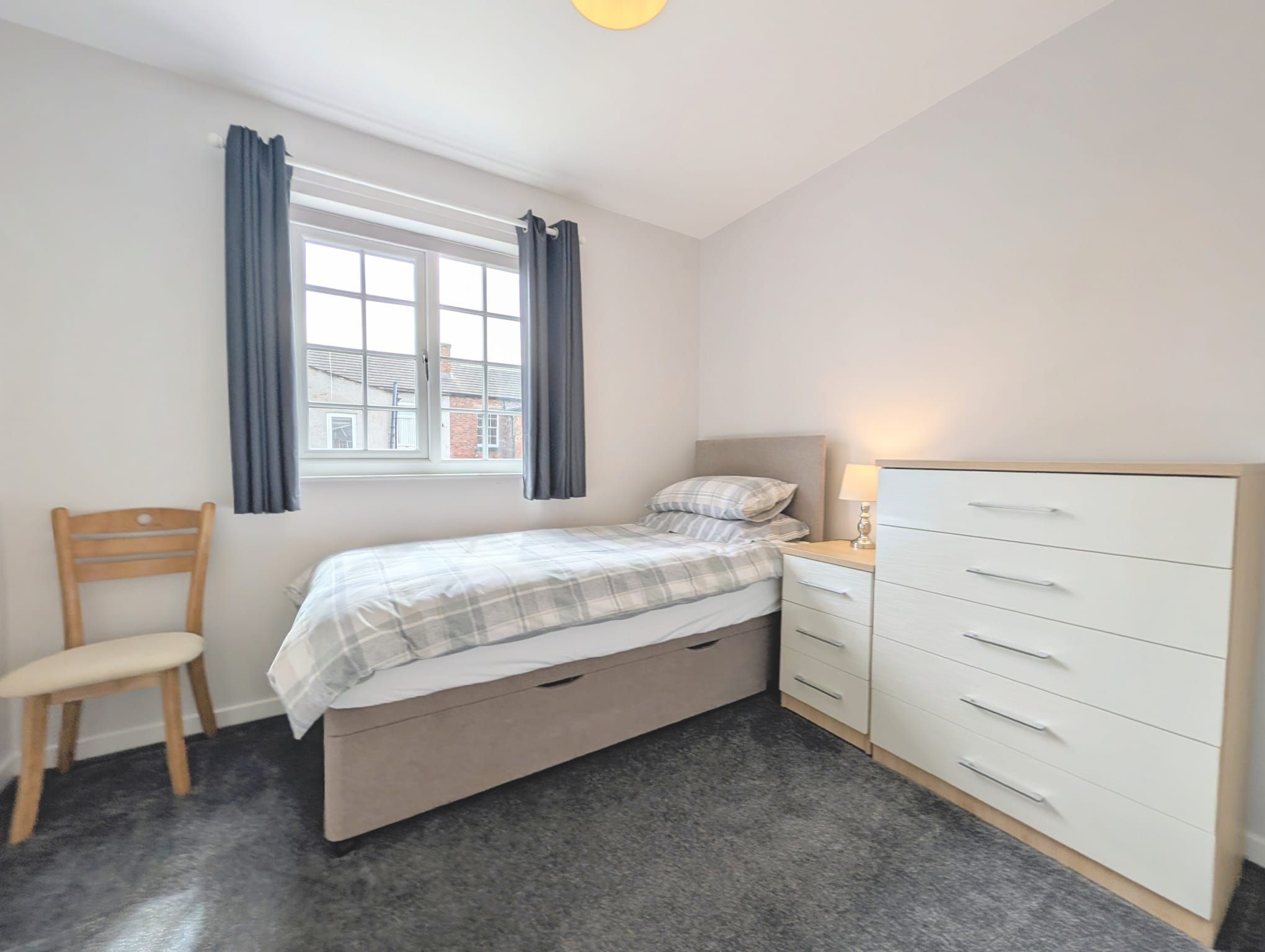 A bedroom with a bed, a chair, a dresser, and a window with curtains.