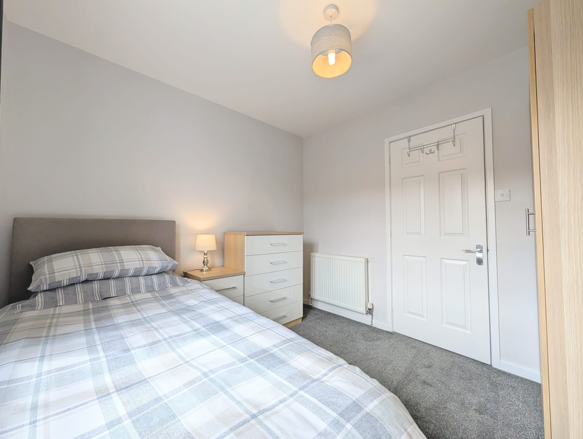 A bedroom with a bed, a nightstand, a dresser, a radiator, and a door.