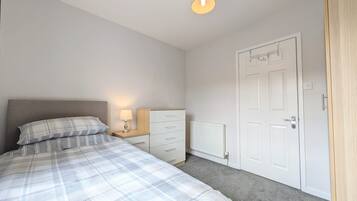 A bedroom with a bed, a nightstand, a dresser, a radiator, and a door.