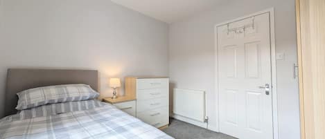 A bedroom with a bed, a nightstand, a dresser, a radiator, and a door.