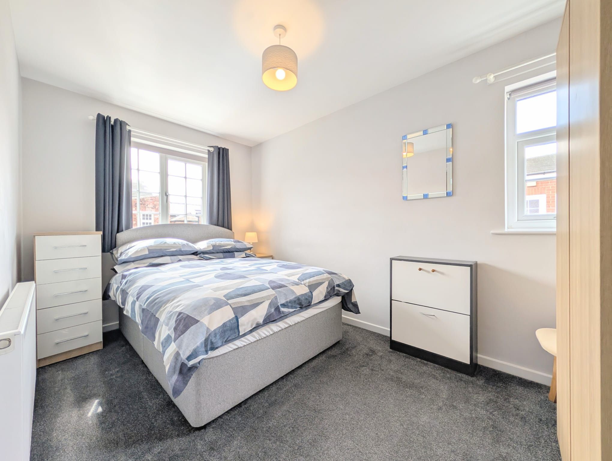 A bedroom with a bed, a bedside table, a dresser, a mirror, and a window.