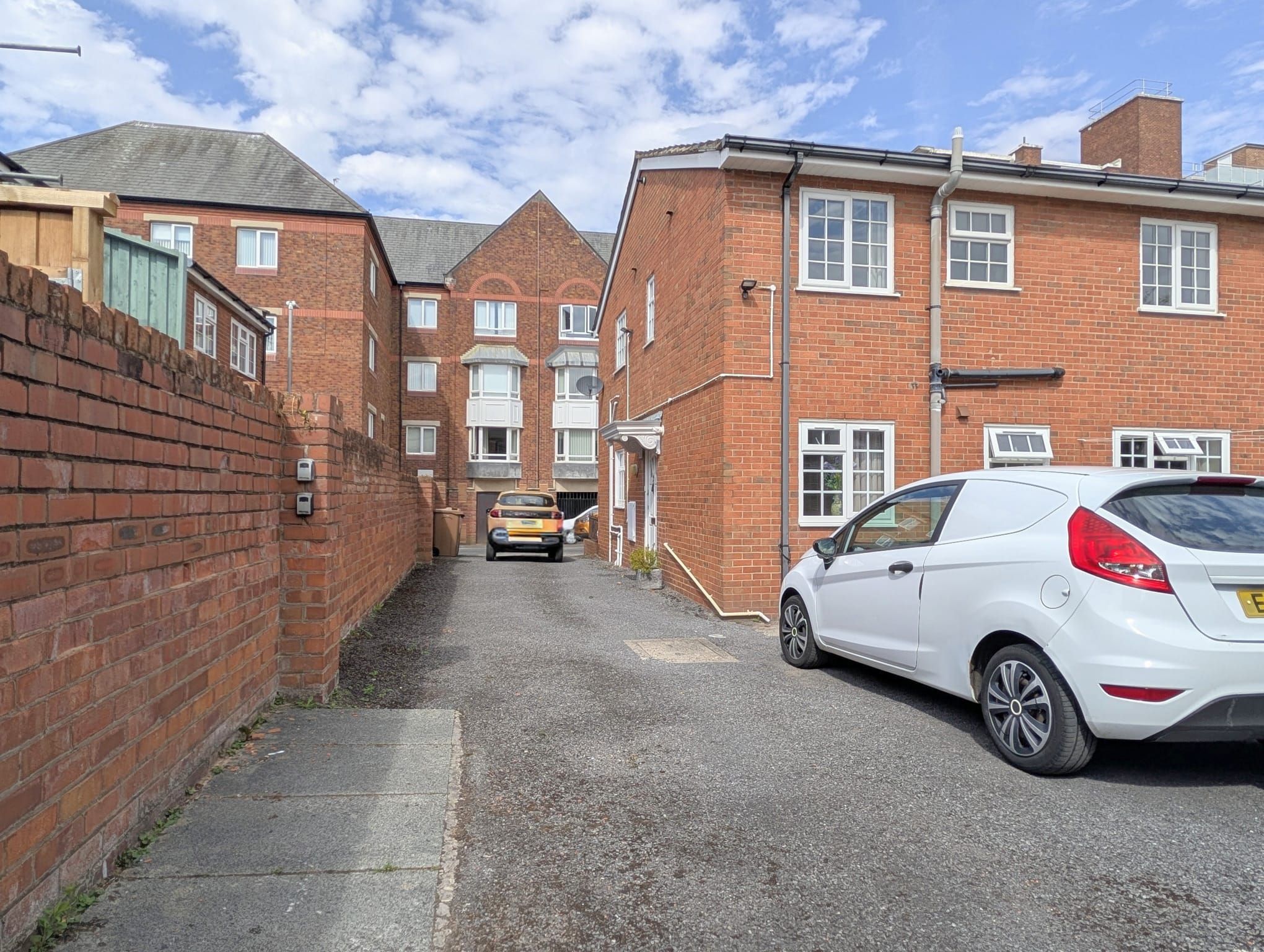 A narrow street with brick buildings, a parked white car, and a yellow vehicle.