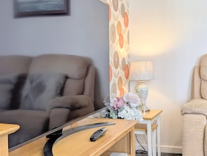 A living room with a sofa, a TV on a stand, a remote control, a lamp, and a small table with flowers. - Stylish Southport Town Centre Retreat + Parking (Southport)