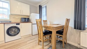 A compact kitchen with a washing machine, microwave, and a dining table with chairs. - Stylish Southport Town Centre Retreat + Parking (Southport)