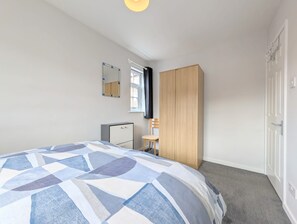 Ein Schlafzimmer mit Bett, Kleiderschrank, Schreibtisch und Spiegel.
