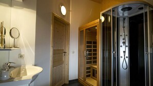 Un baño moderno con ducha envuelta en vidrio, puerta de madera y lavamanos blanco.