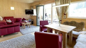 Interior acogedor de una cabaña con techo de madera, un sofá rojo, una mesa de comedor y un televisor.