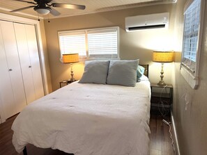A bedroom with a bed, two bedside lamps, an air conditioning unit, a ceiling fan, and a window with blinds. - Lakefront 2-bedroom home on Palo Pinto Lake with Fishing Dock (Gordon)