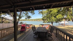 Un espacio de estar al aire libre con techo y vistas a un lago, muelle de madera y una bandera.