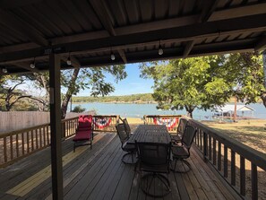 A covered outdoor seating area with a view of a lake, wooden deck, and a flag. - Lakefront 2-bedroom home on Palo Pinto Lake with Fishing Dock (Gordon)