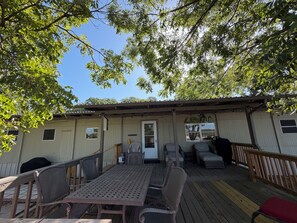 A covered outdoor deck with a table and chairs, a small seating area with cushions, and a sign that reads 'Lake Cottage.' - Lakefront 2-bedroom home on Palo Pinto Lake with Fishing Dock (Gordon)