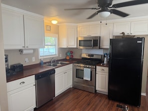 A kitchen with white cabinets, a stainless steel microwave, a black refrigerator, a dishwasher, and a ceiling fan. - Lakefront 2-bedroom home on Palo Pinto Lake with Fishing Dock (Gordon)