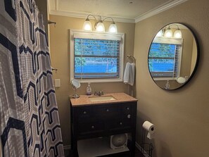 A bathroom with a vanity, a mirror, a window with blinds, a towel rack, and a toilet paper holder. - Lakefront 2-bedroom home on Palo Pinto Lake with Fishing Dock (Gordon)