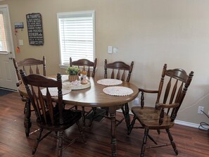 Une salle à manger avec une table ronde en bois, entourée de six chaises, d’une plante en pot et de sets de table.