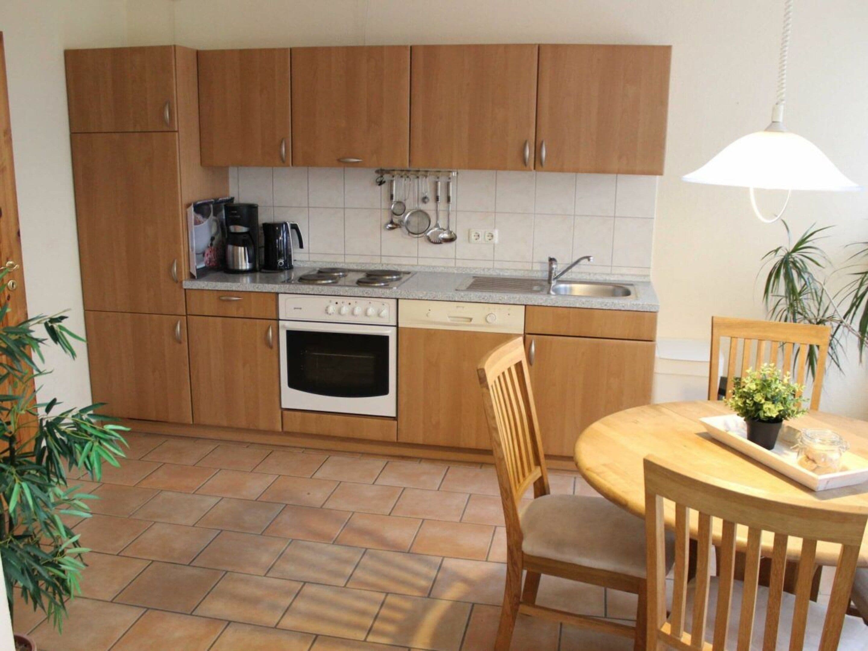 Une cuisine compacte dotée de meubles en bois, d’une cuisinière, d’un four, d’un évier et d’un coin repas avec une table et des chaises.