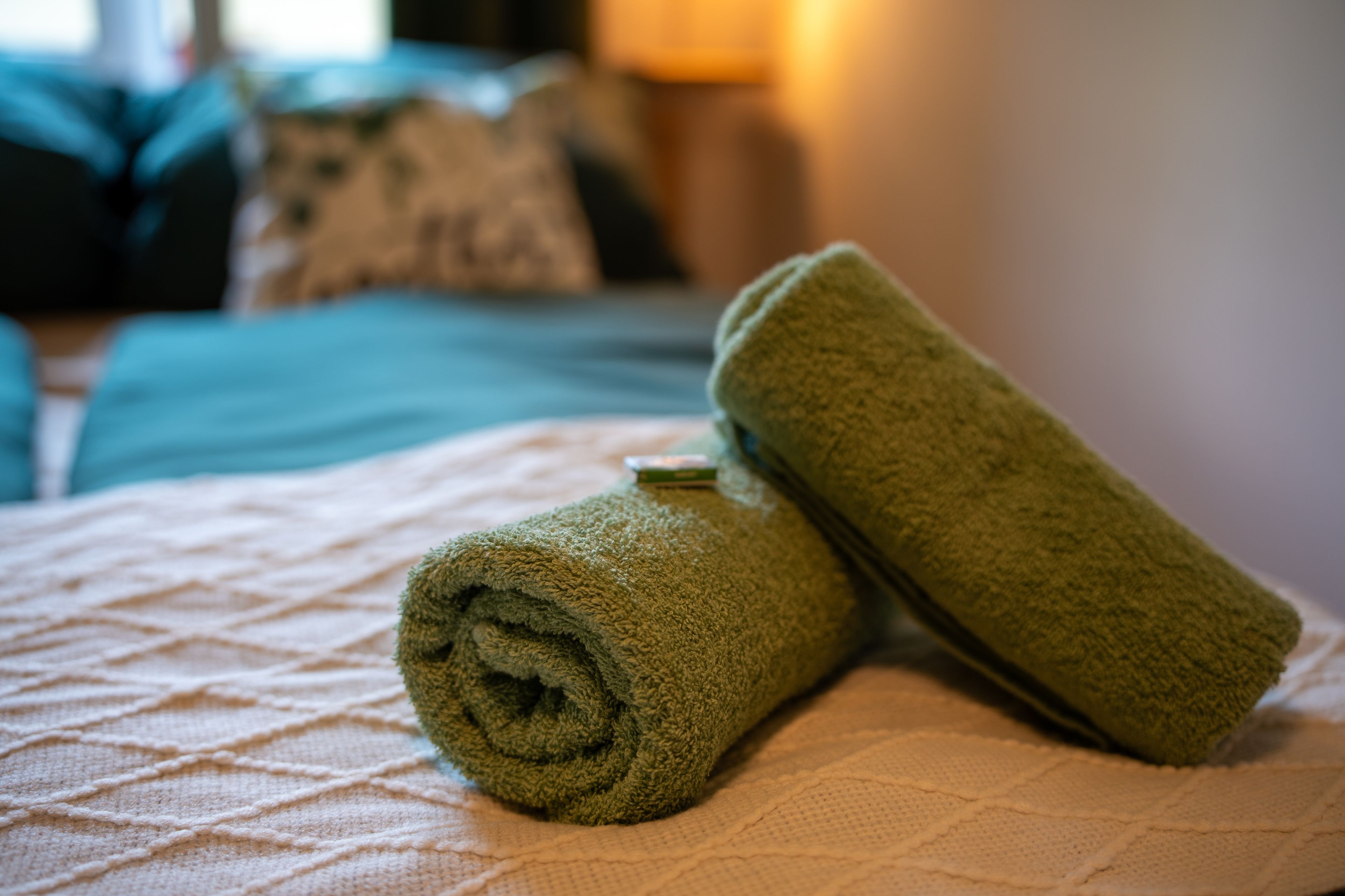 A bed with a rolled-up green towel and a pillow.