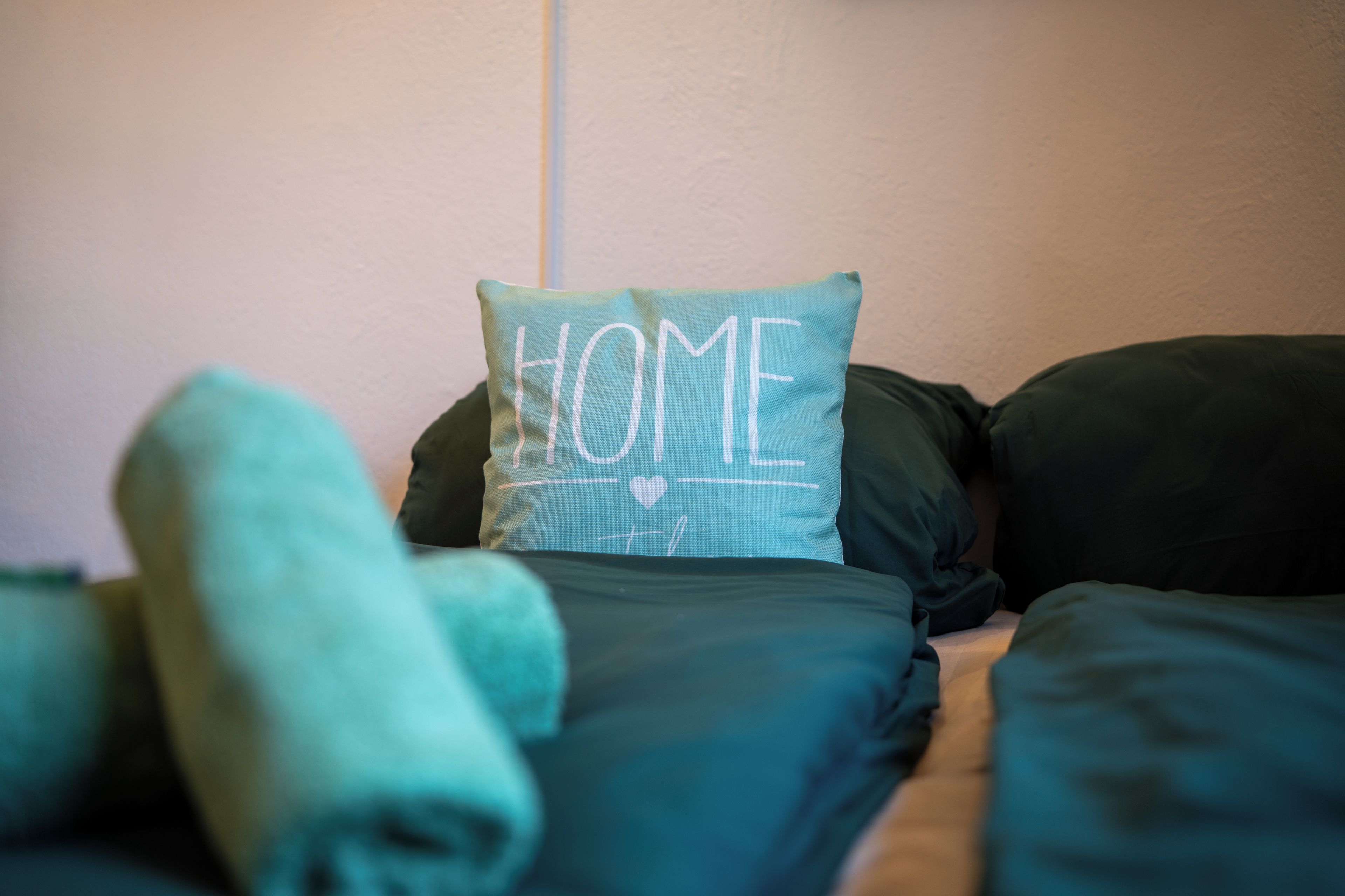 Un letto con un cuscino con la scritta 'HOME' e asciugamani arrotolati.
