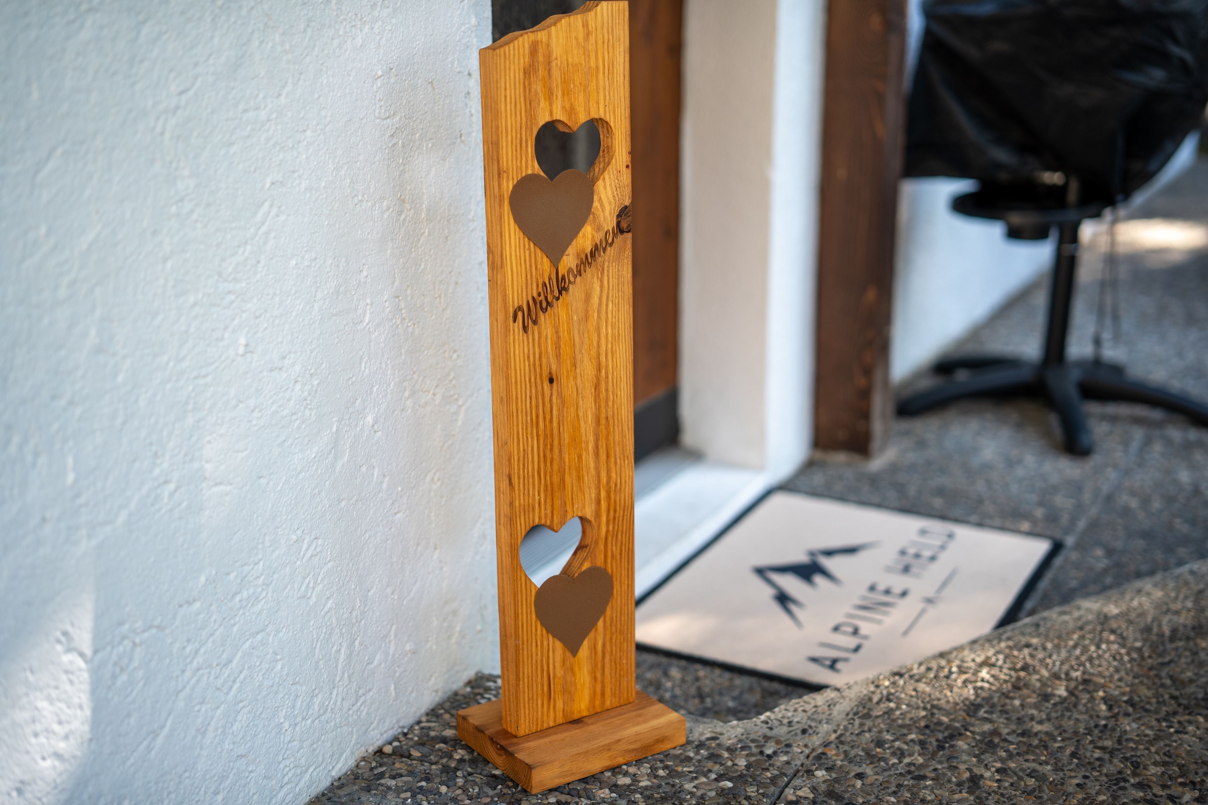 A wooden sign with heart cutouts and the word 'Willkommen' engraved, placed on a stone surface.