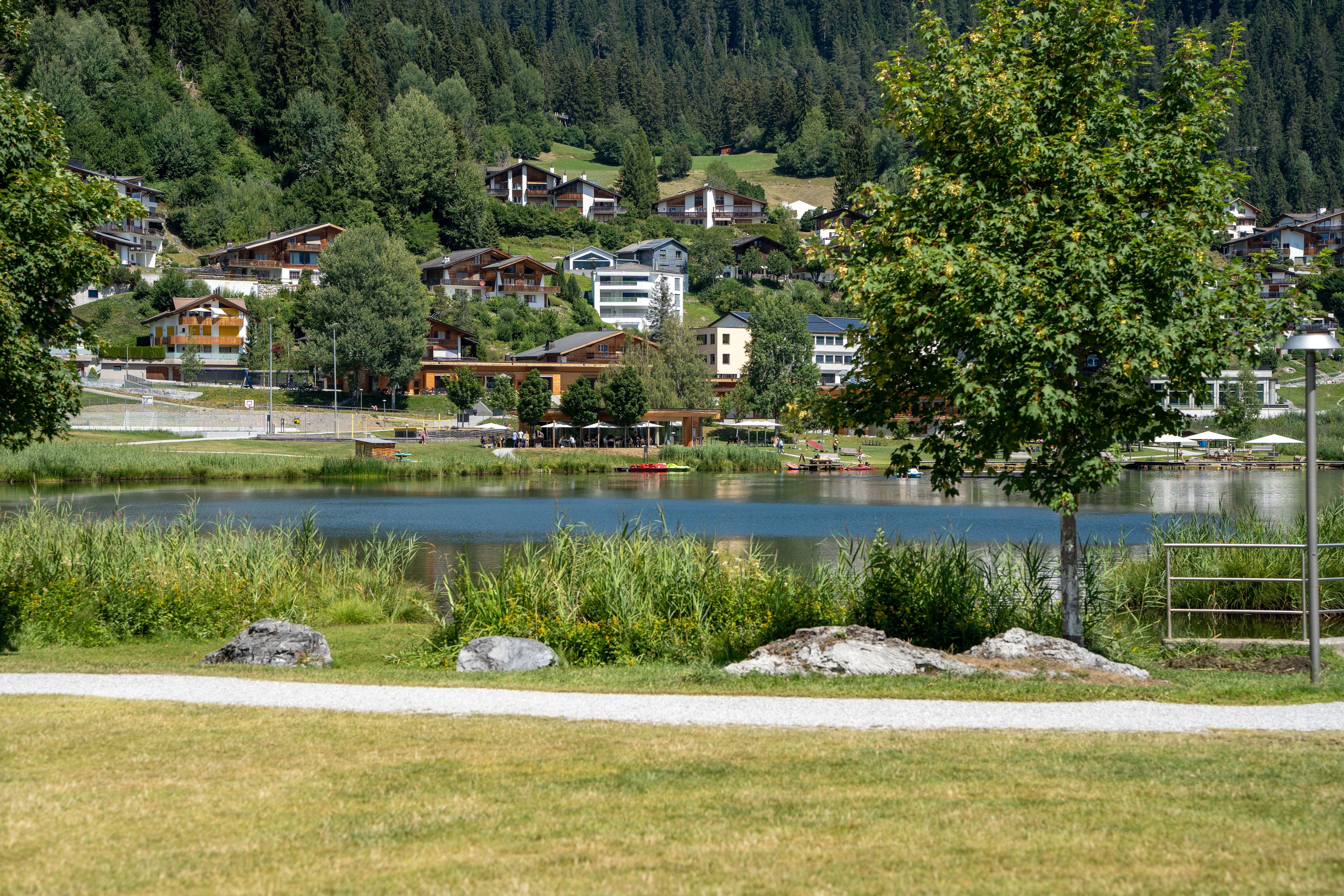 Vista de un lago con casas, un sendero y un muelle con barcos.
