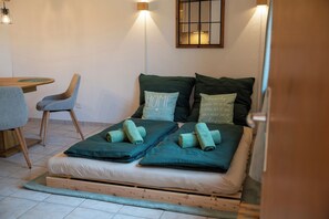 A single bed with two pillows, a wooden headboard, and a small table with a chair in a room with white walls and a window. - Alpenwohnung in Laax Garten, Bergblick & Parkplatz (Laax)