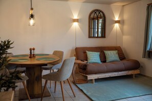 A cozy living room with a brown sofa, a dining table with chairs, and a small window with a view.