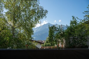 A mountain landscape with a clear sky, a wooden fence, and buildings in the foreground.