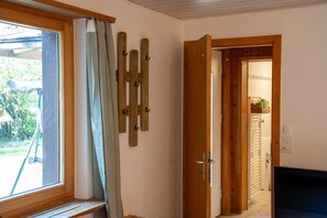 A room with a wooden door, a window with curtains, and a wall-mounted wooden rack.