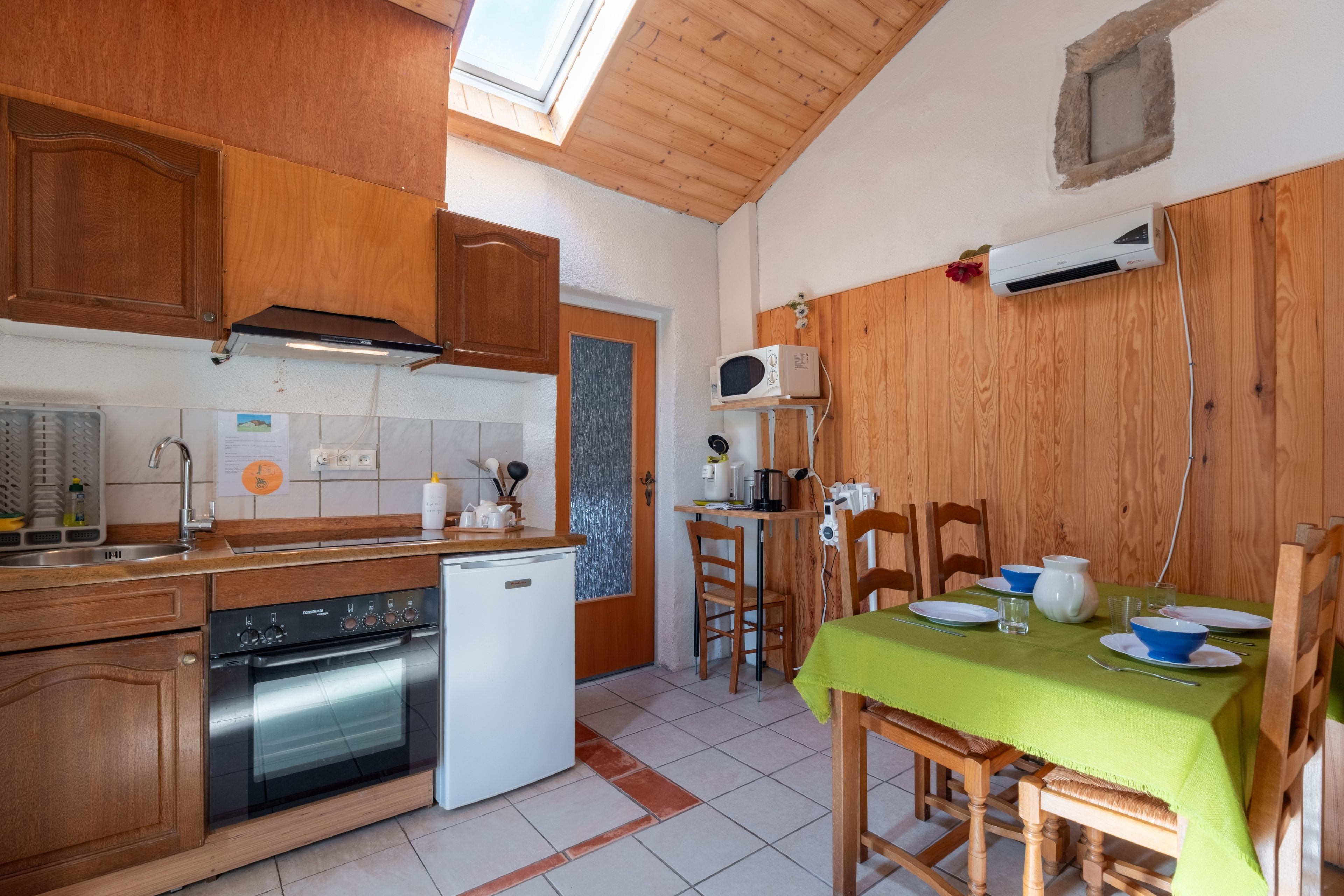 Uma cozinha compacta com armários de madeira, forno embutido, micro-ondas e um espaço de refeições com mesa posta para dois.