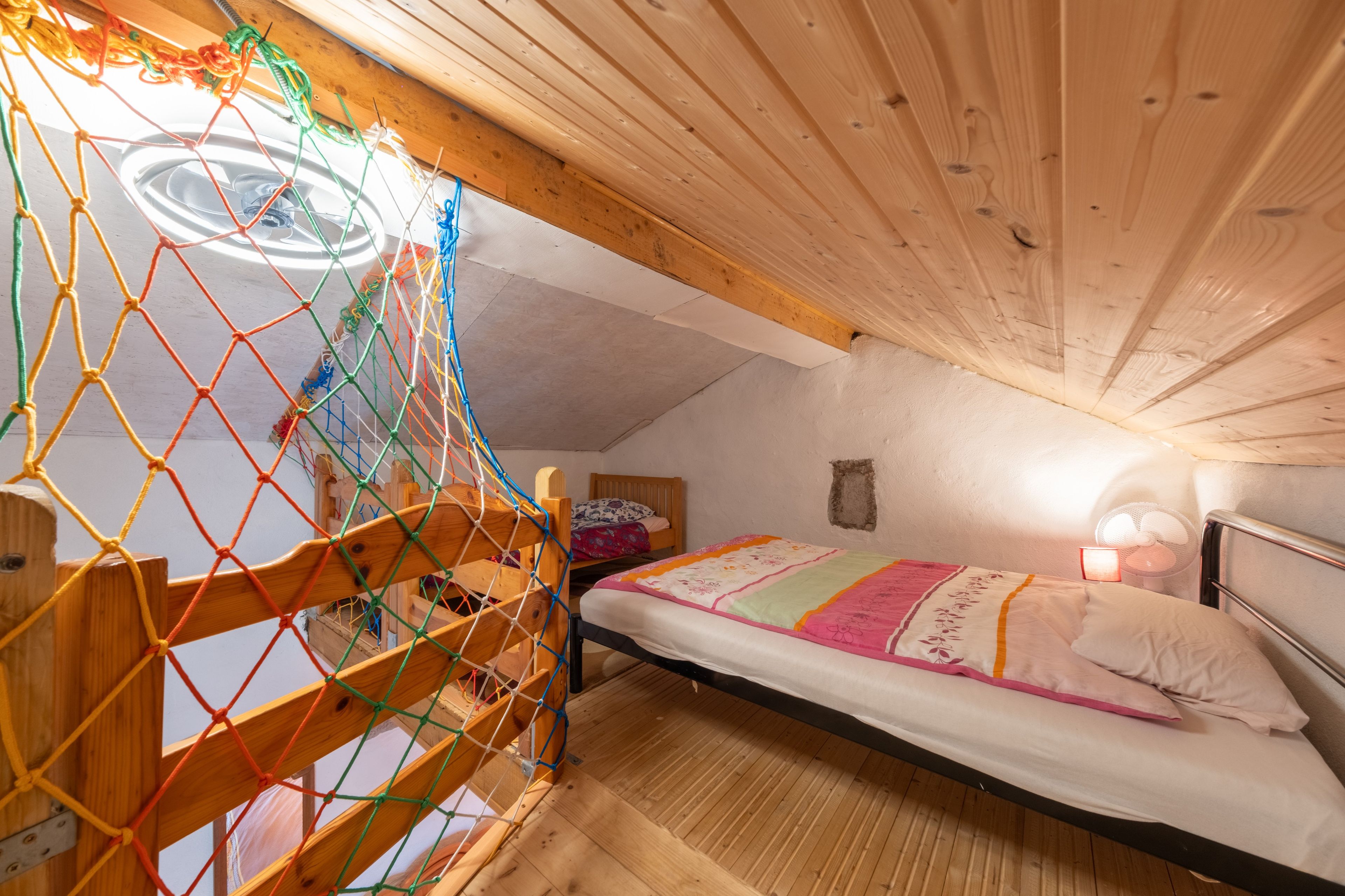 Quarto com teto de madeira, cama com colcha colorida e um espaço infantil com mosquiteiro.