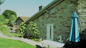 A stone building with a door, a table, chairs, and a blue umbrella. - Maison Principale Apartment: Mountain View, Private Terrace, and Wi-Fi (Xertigny)