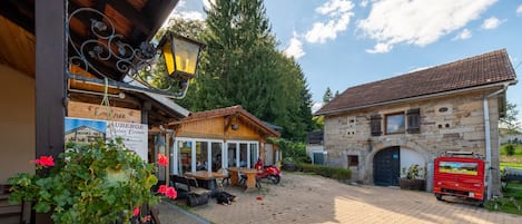 Ein Innenhof mit einem Holzgebäude, einem Steinhaus und einem roten Fahrzeug davor.