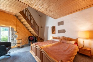 Makuuhuoneessa on puinen sänky, yöpöytä, lamppu, tuoli, työpöytä ja portaat.