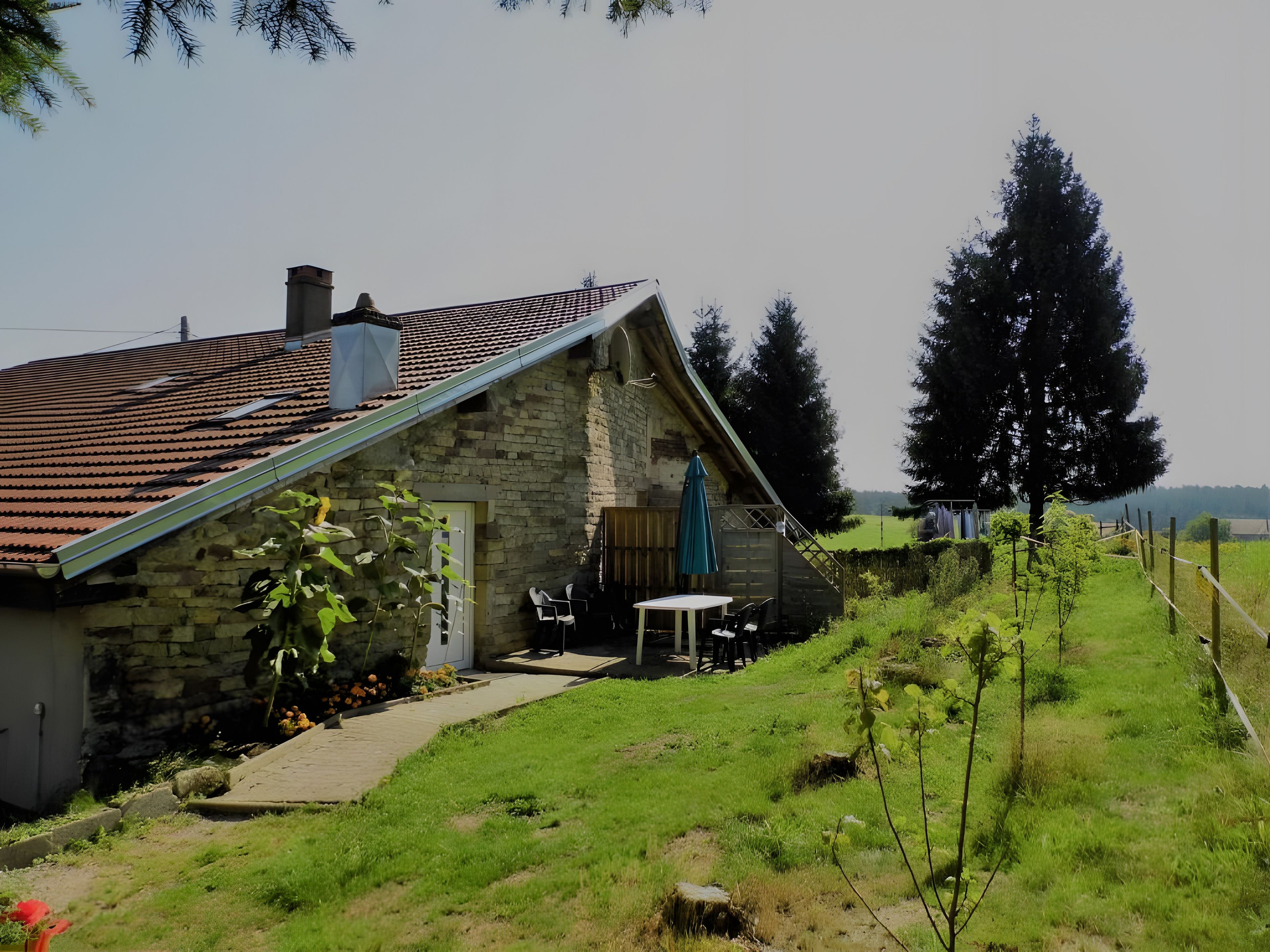 Een stenen huis met een schuin dak, een terras met zitplaatsen en uitzicht op het landschap.