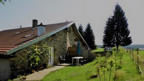 A stone house with a sloped roof, a patio with outdoor seating, and a view of the countryside. - Maison Principale Apartment: Mountain View, Private Terrace, and Wi-Fi (Xertigny)