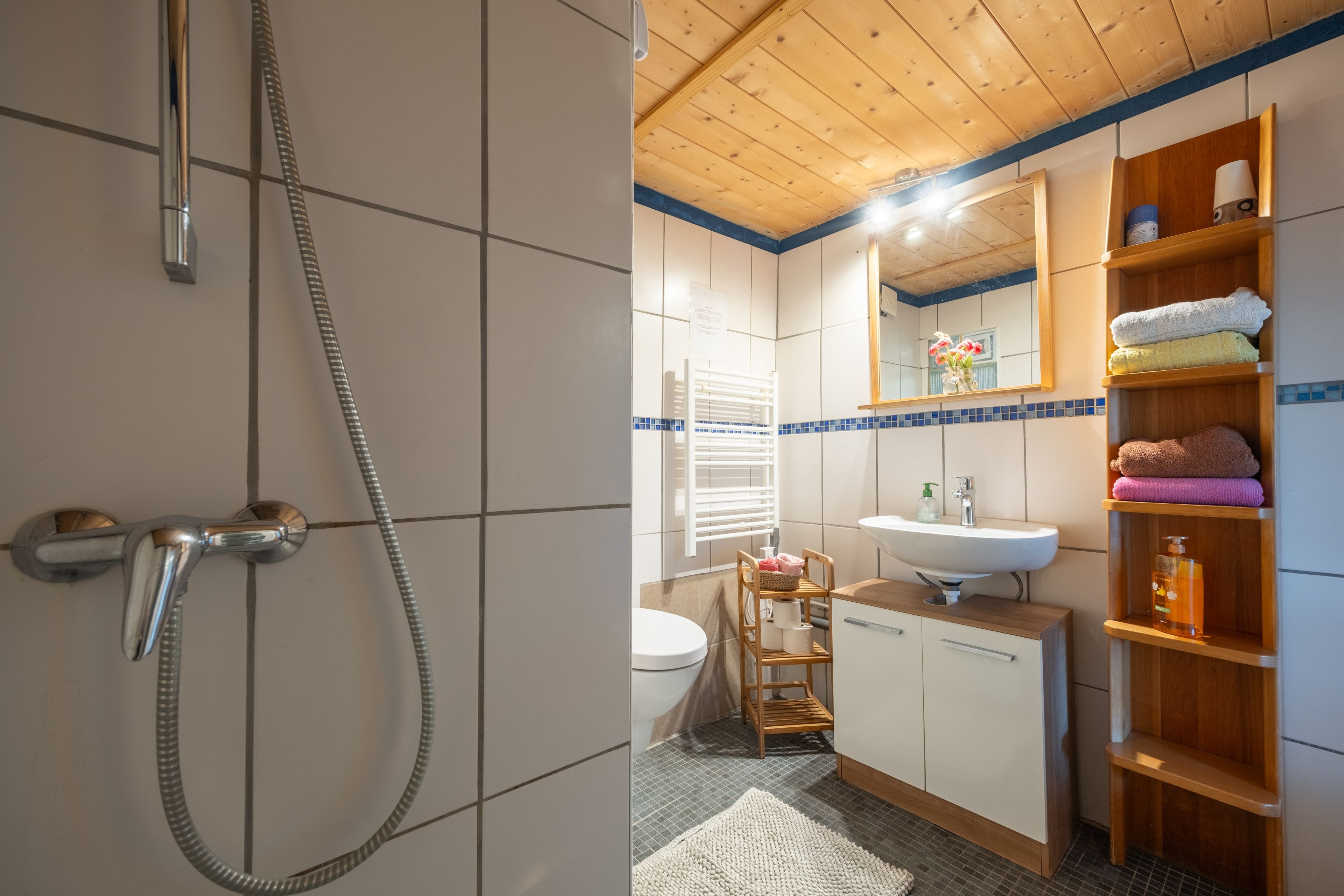 Une salle de bain équipée d’une douche, de toilettes, d’un lavabo et d’étagères en bois où sont rangées les serviettes.