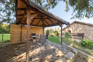 A covered patio area with a stone floor, wooden furniture, and a stone building in the background. - Apartment 'Maison Du Bonheur - Appartement' with Mountain View, Private Terrace and Wi-Fi (Xertigny)