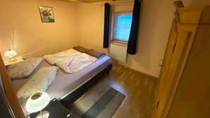 A small, cozy room with a bed, a desk, a lamp, and a window with curtains. - Apartment 'Maison Du Bonheur - Appartement' with Mountain View, Private Terrace and Wi-Fi (Xertigny)
